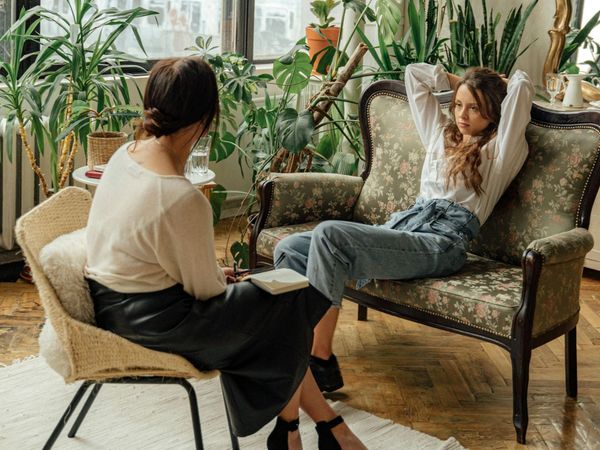 A woman is sitting on a couch talking to another woman.