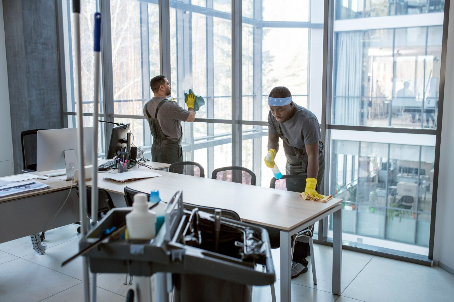 Two men are cleaning an office with cleaning supplies.