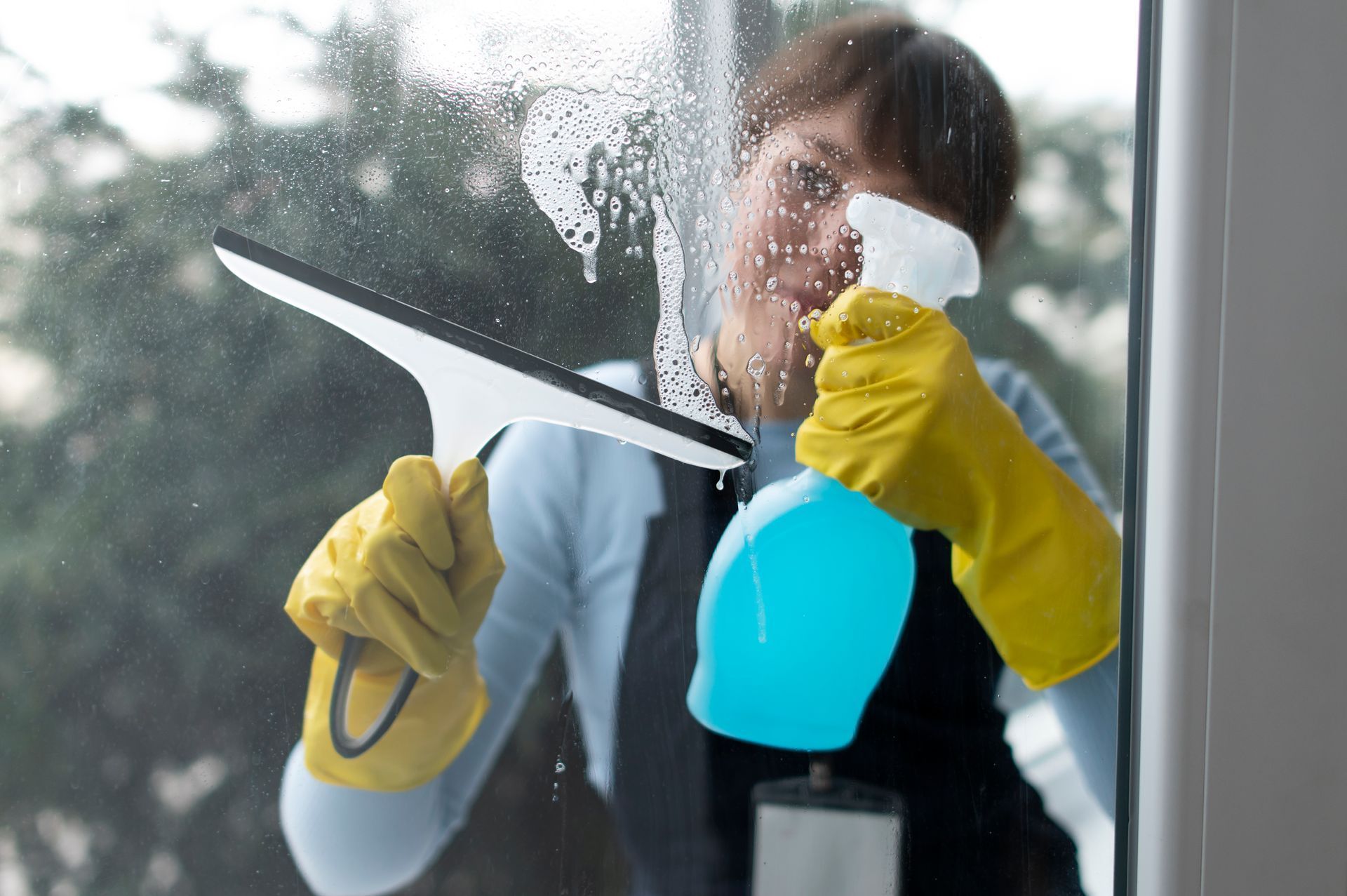 A woman is cleaning a window with a squeegee and spray bottle.