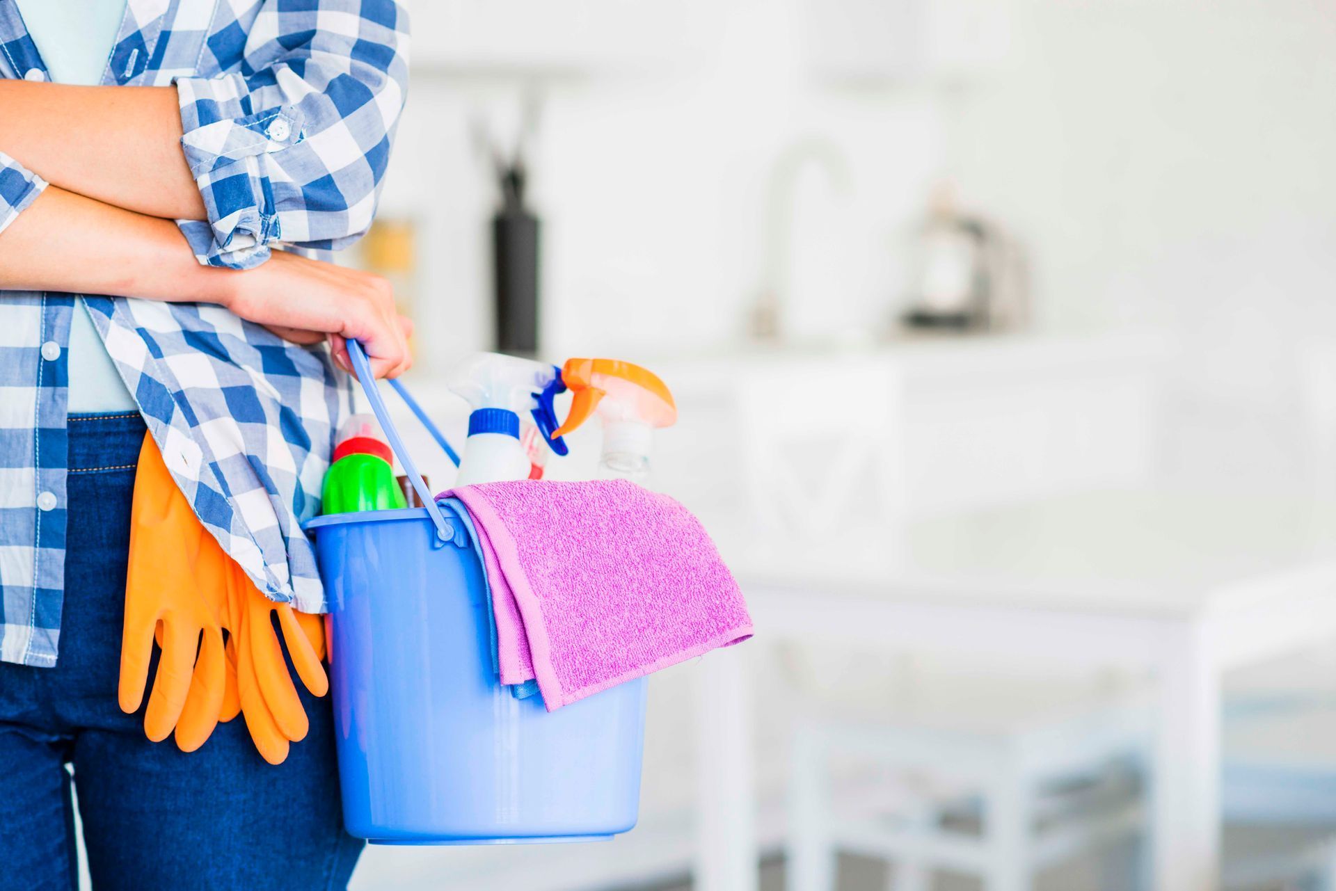 A woman is holding a bucket of cleaning supplies in a kitchen.