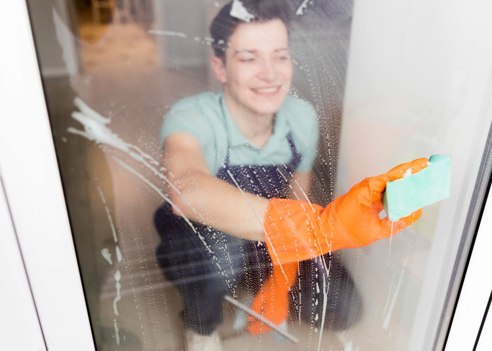 A woman in orange gloves is cleaning a window with a sponge.