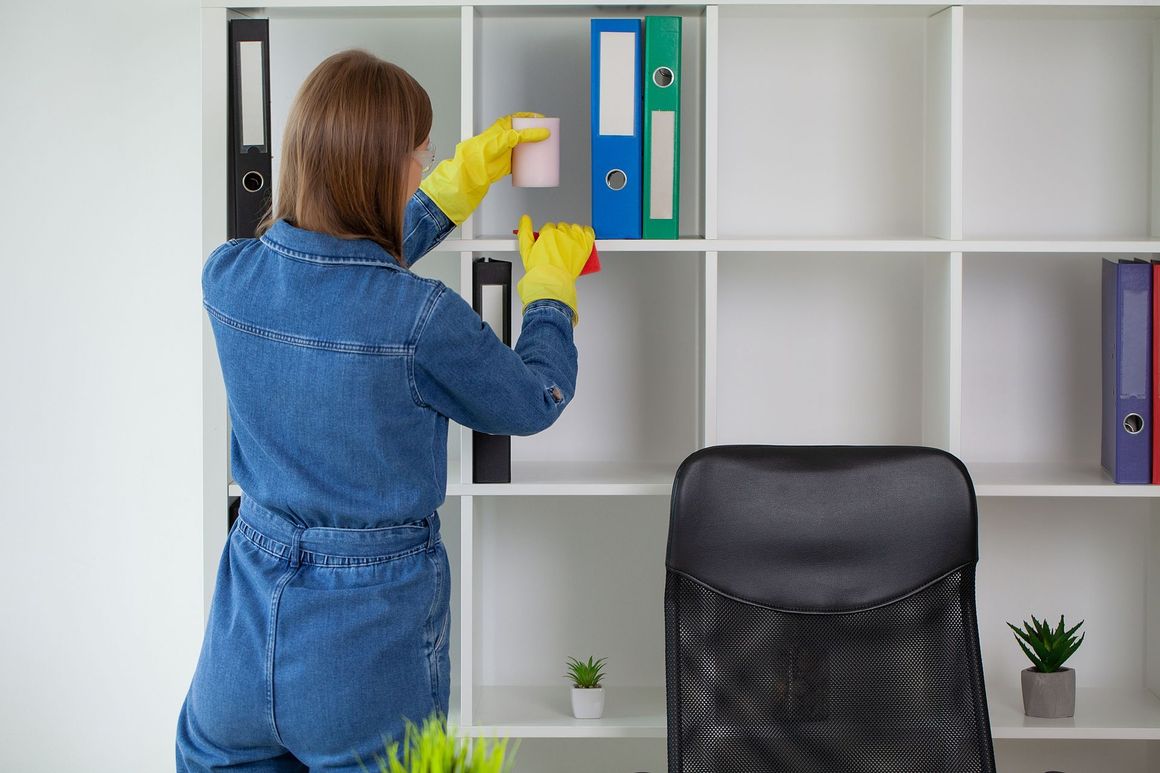 A woman in yellow gloves is cleaning a shelf in an office.