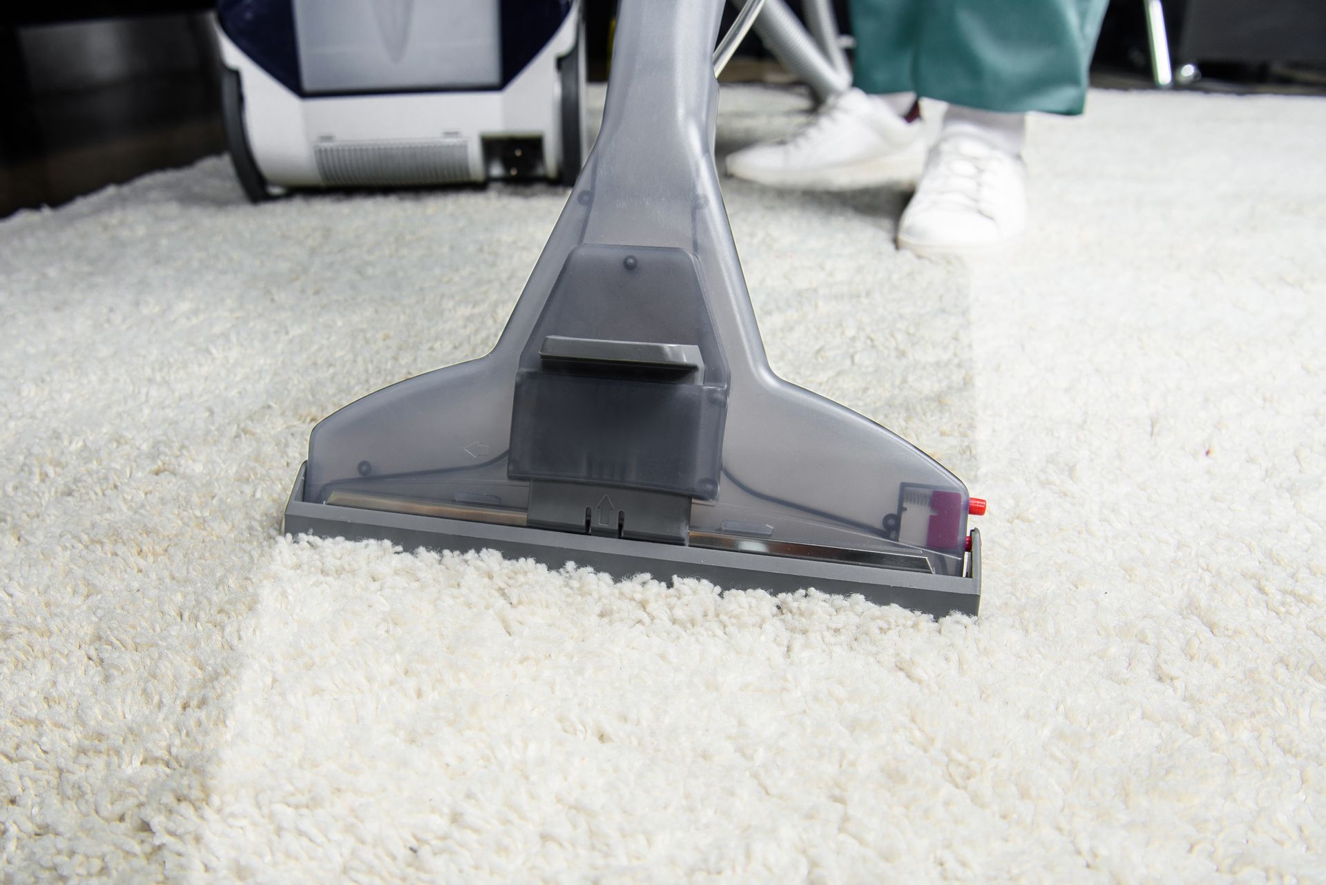 A person is using a vacuum cleaner to clean a white carpet.