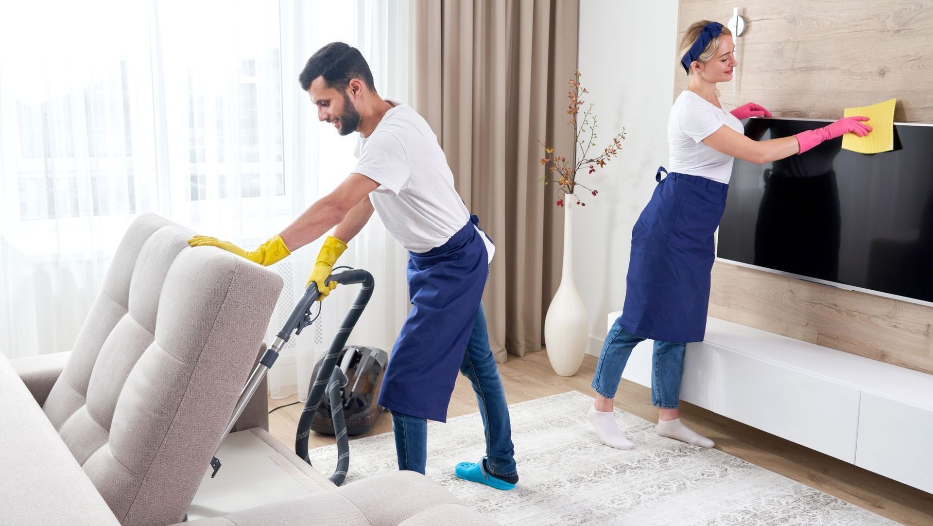 A man and a woman are cleaning a living room.