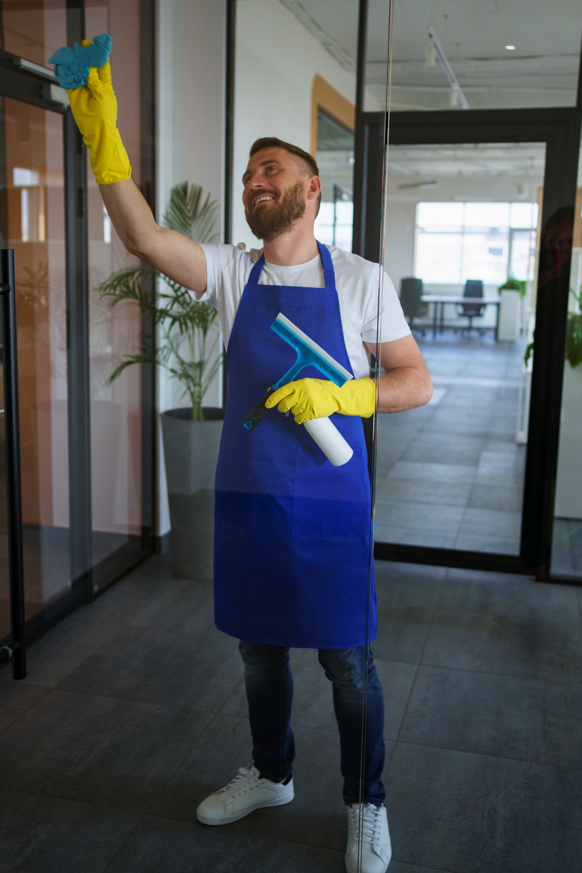 A man in an apron is cleaning a window in an office.