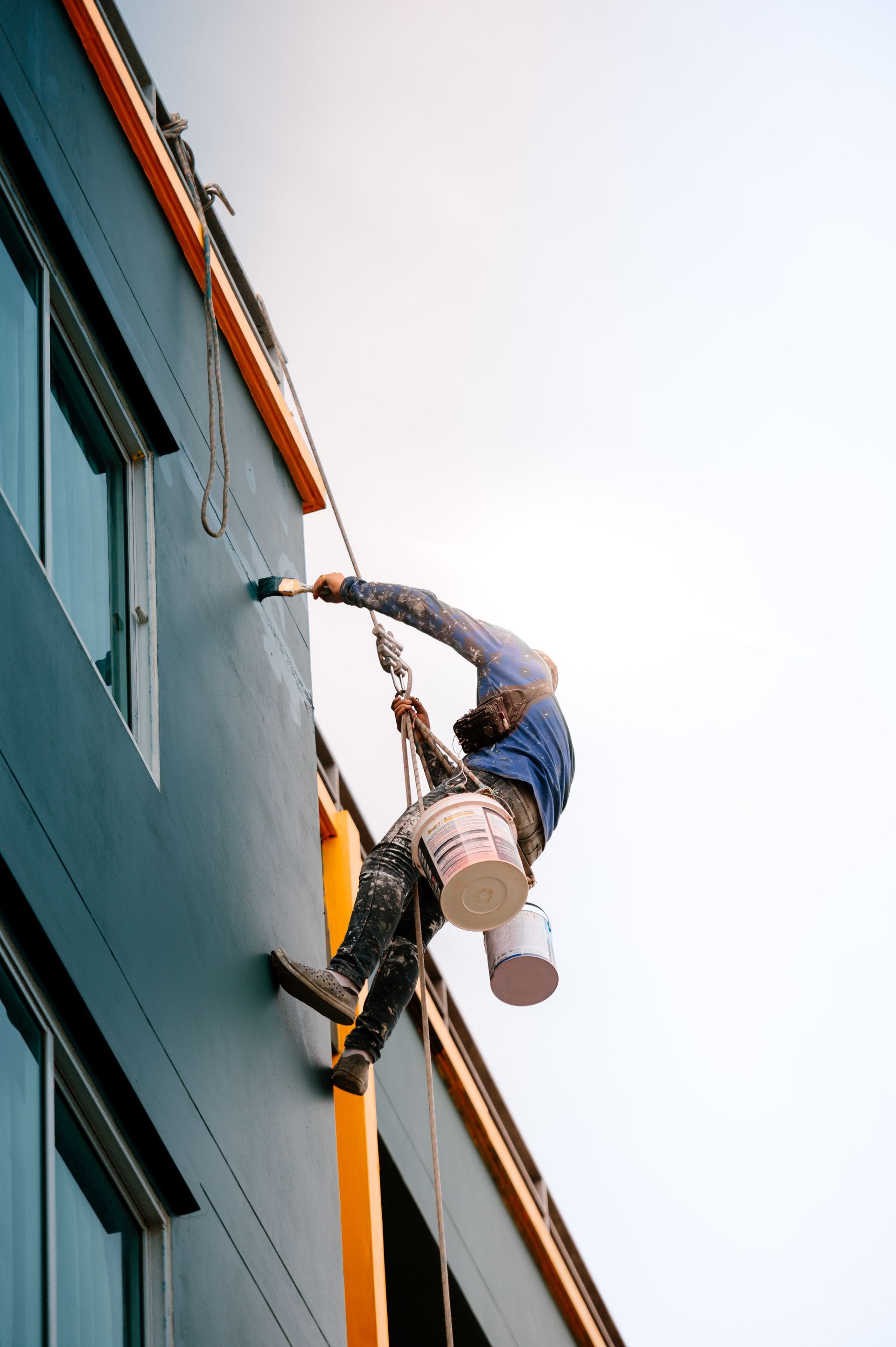 A man is painting the side of a building with a bucket.