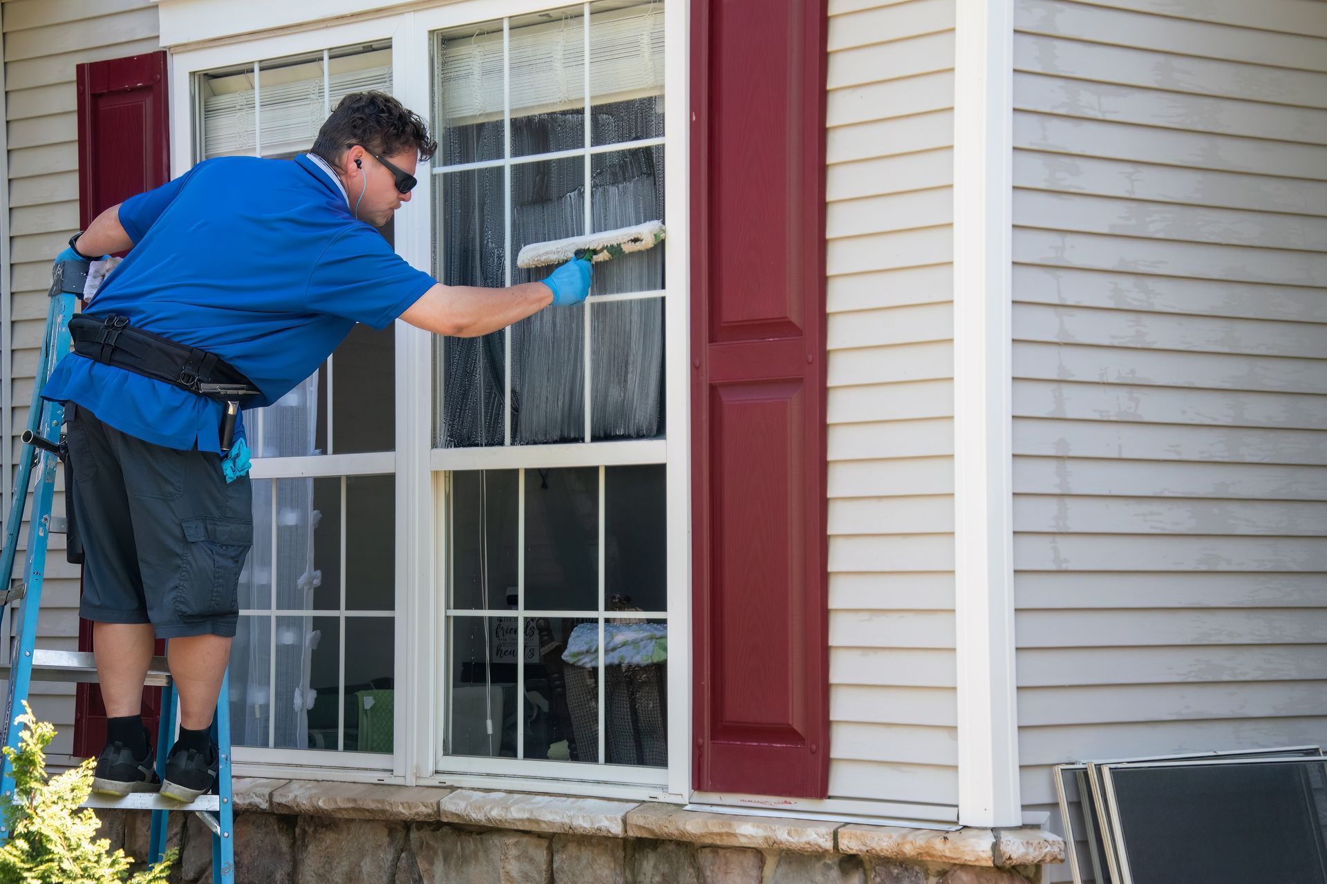 A man is standing on a ladder cleaning a window of a house.