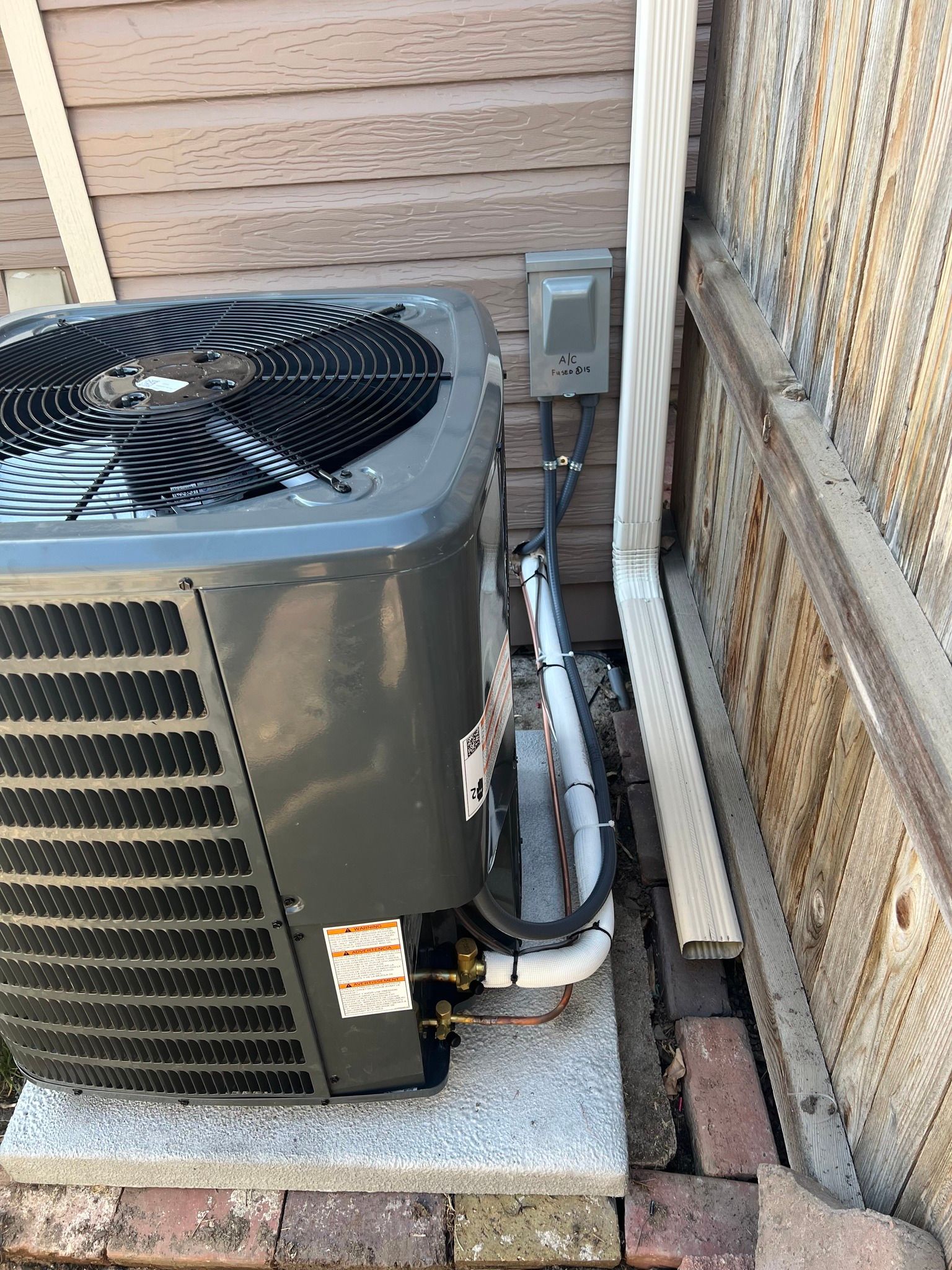 Comfy Castle Heating and Air - An air conditioner is sitting on top of a brick wall next to a wooden fence.
