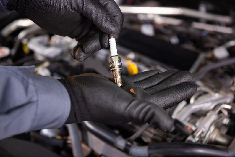 A person is holding a spark plug in their hand in front of a car engine.