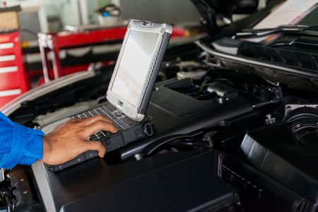 A person is using a laptop computer under the hood of a car.