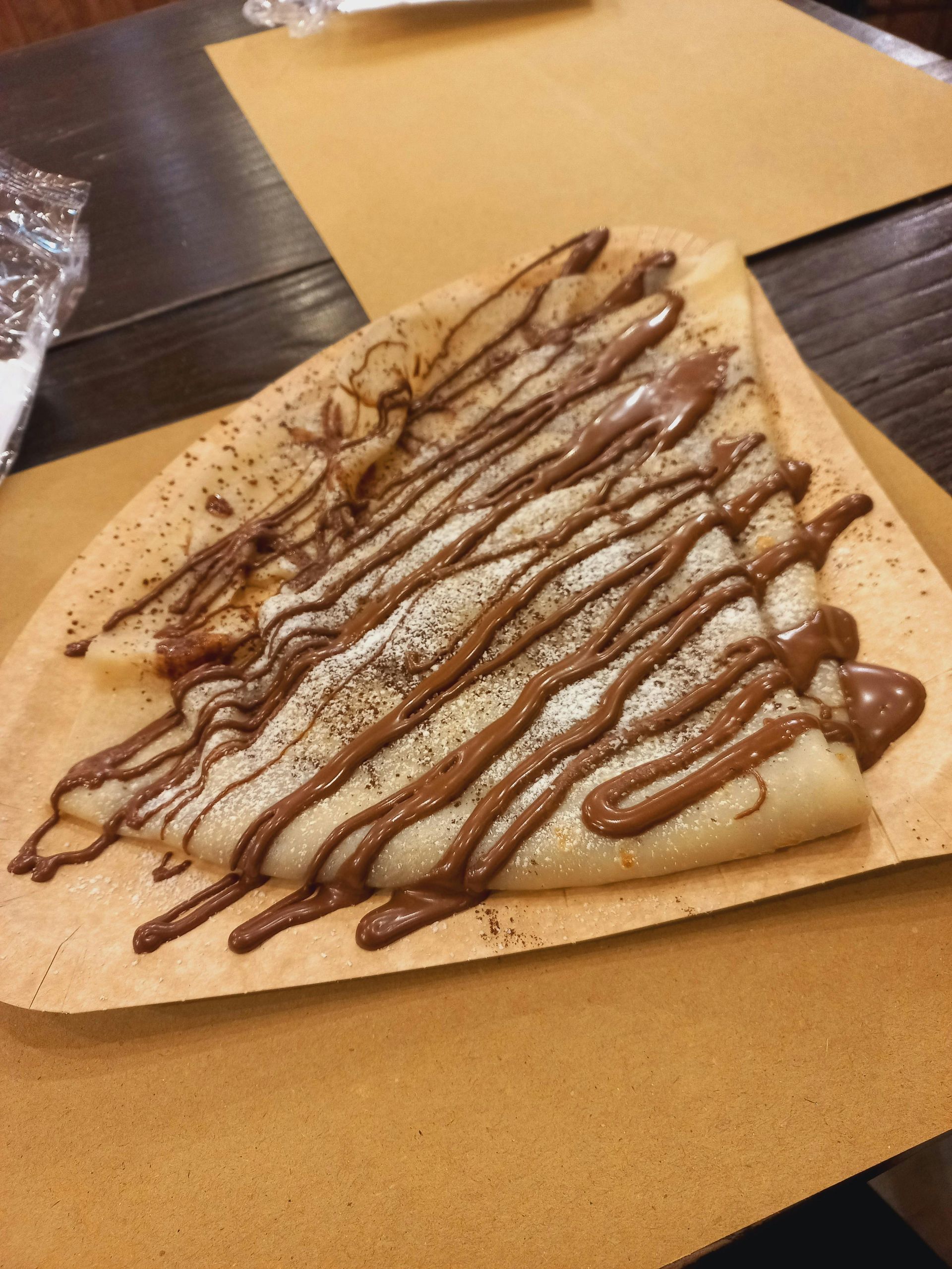 Crêpe con salsa e polvere di cioccolato servita su un foglio di carta.