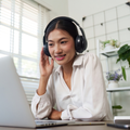 Woman wearing headphones smiles at a laptop in a bright home office