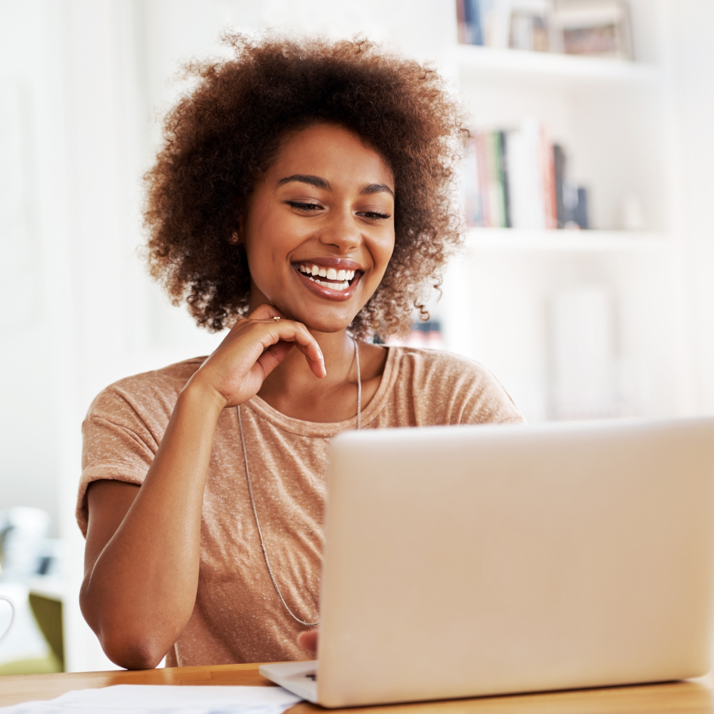 Smiling person using a laptop at a desk in a bright room