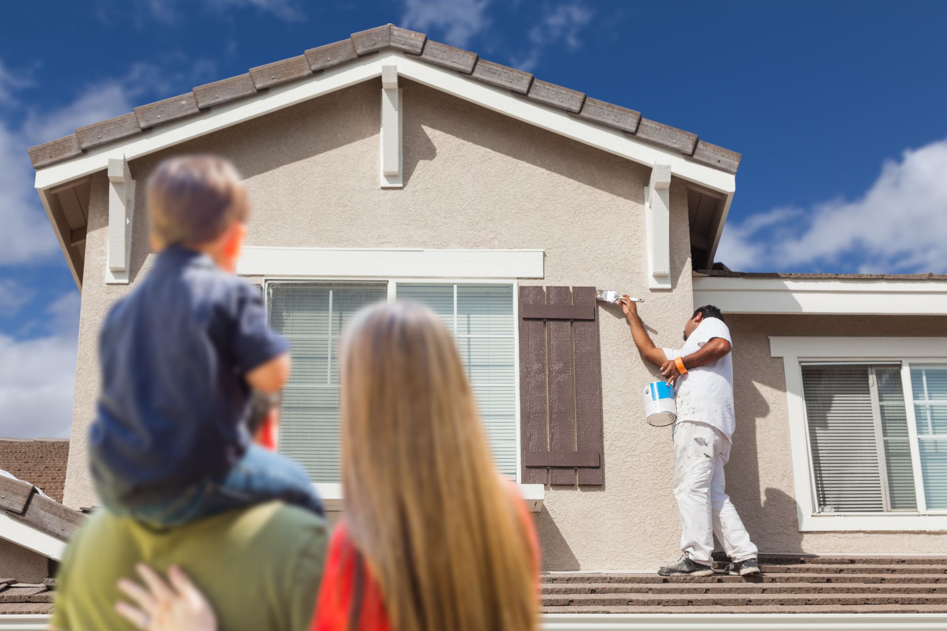 A family is looking at a man painting their house.