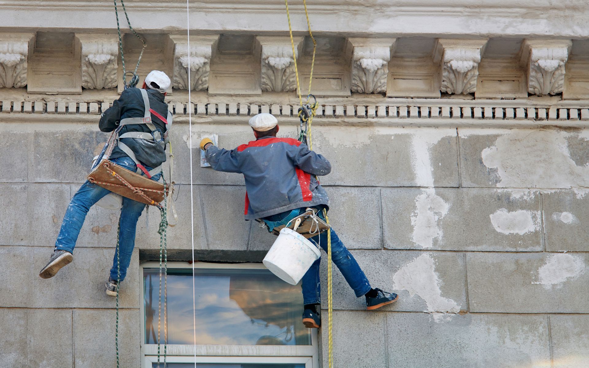 Two men are painting the side of a building.