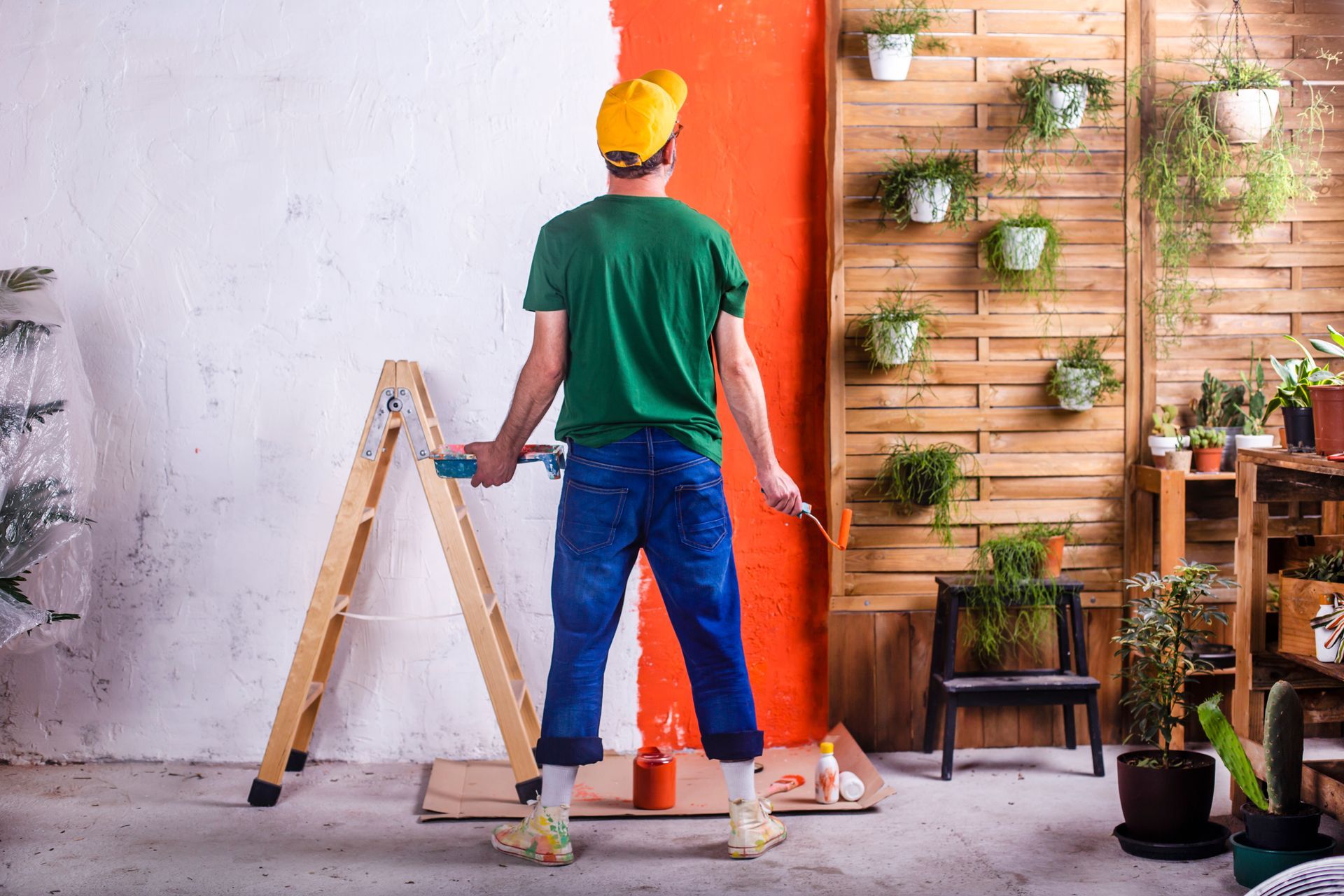 A man is standing next to a ladder painting a wall diy.