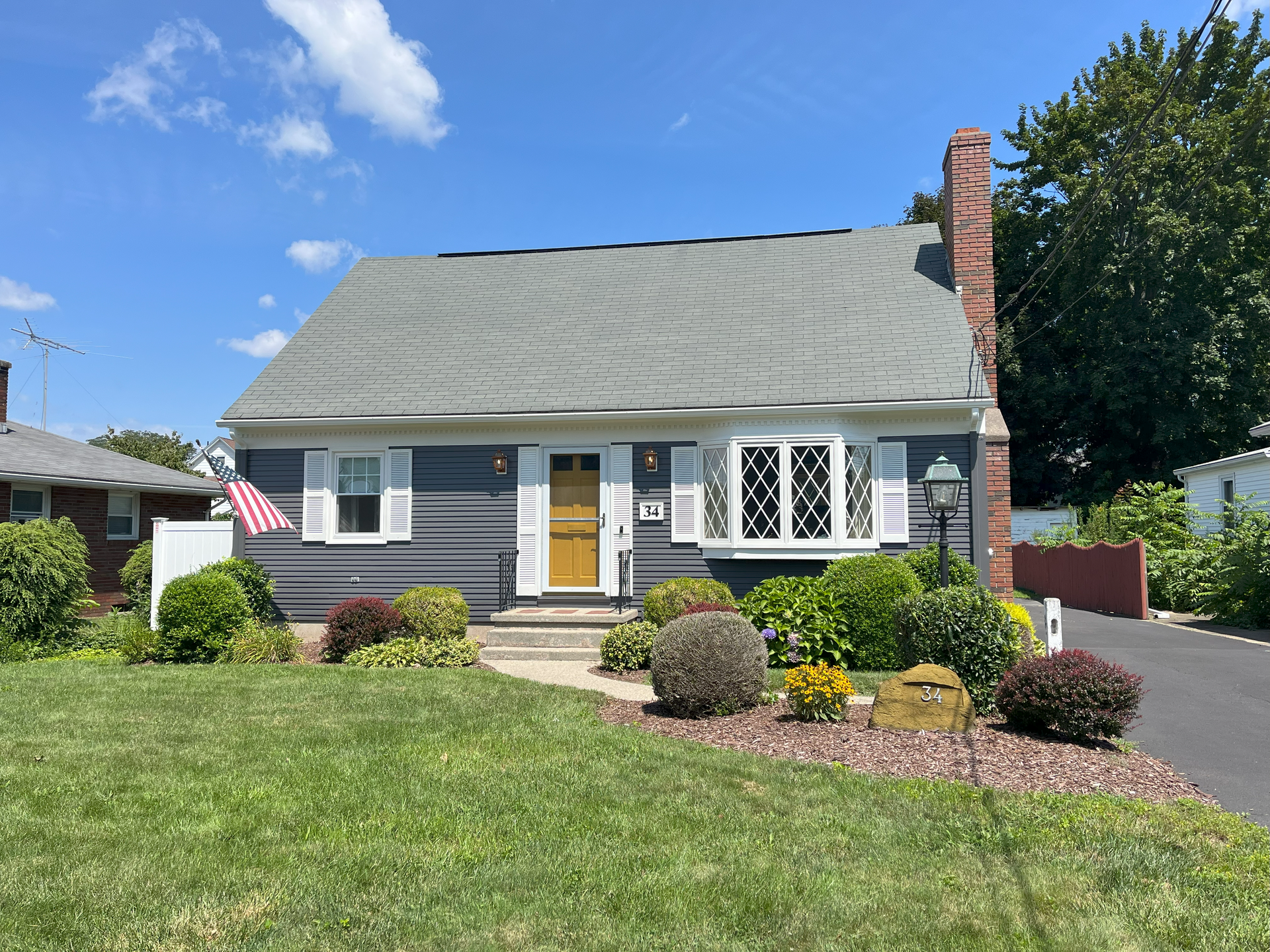 a house with a gray roof and white shutters is sitting on top of a lush green law. exterior home painting after project