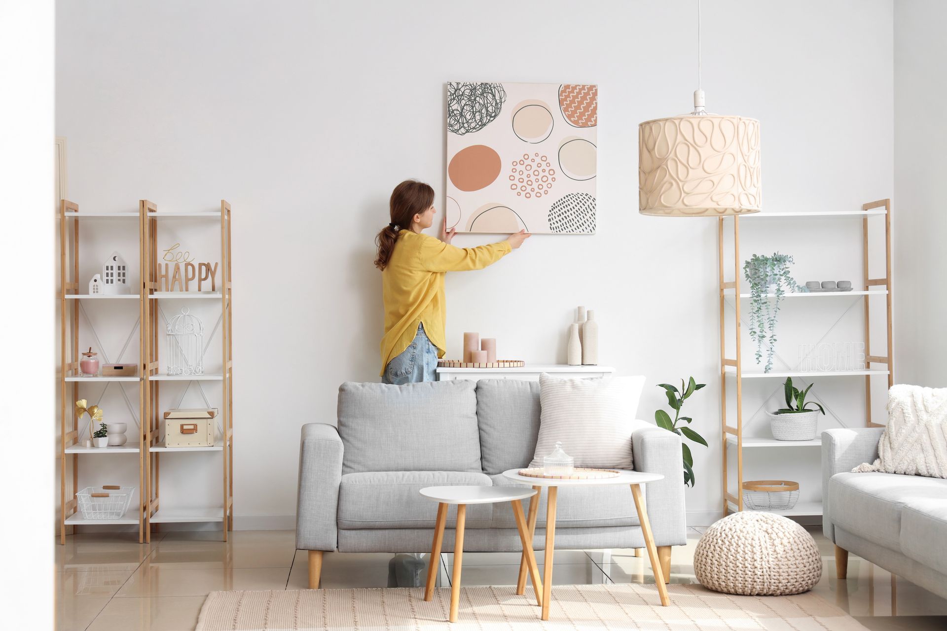 A woman is hanging a painting on a wall in a living room.