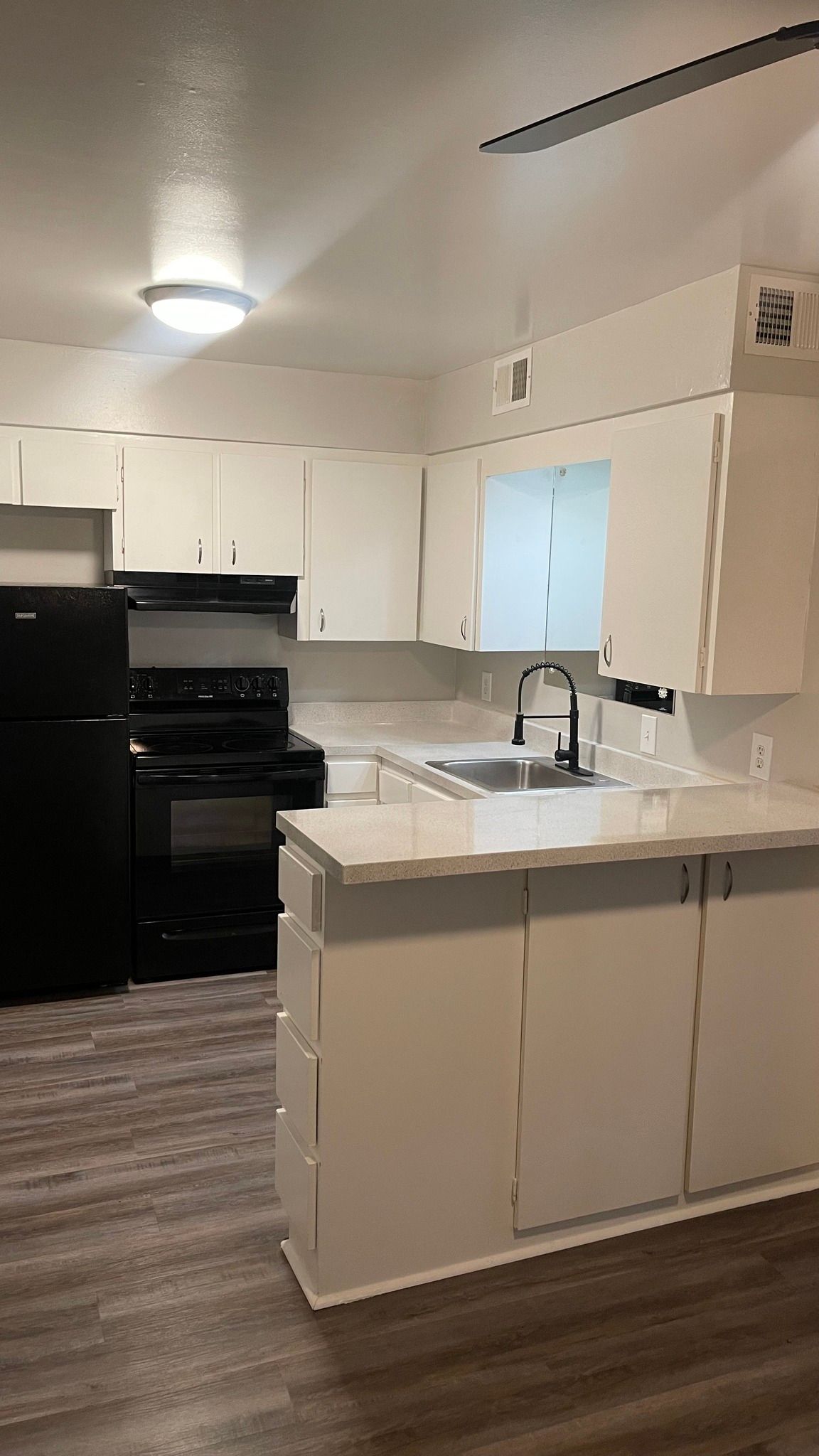 A kitchen with white cabinets , a black refrigerator , a black stove , and a sink.