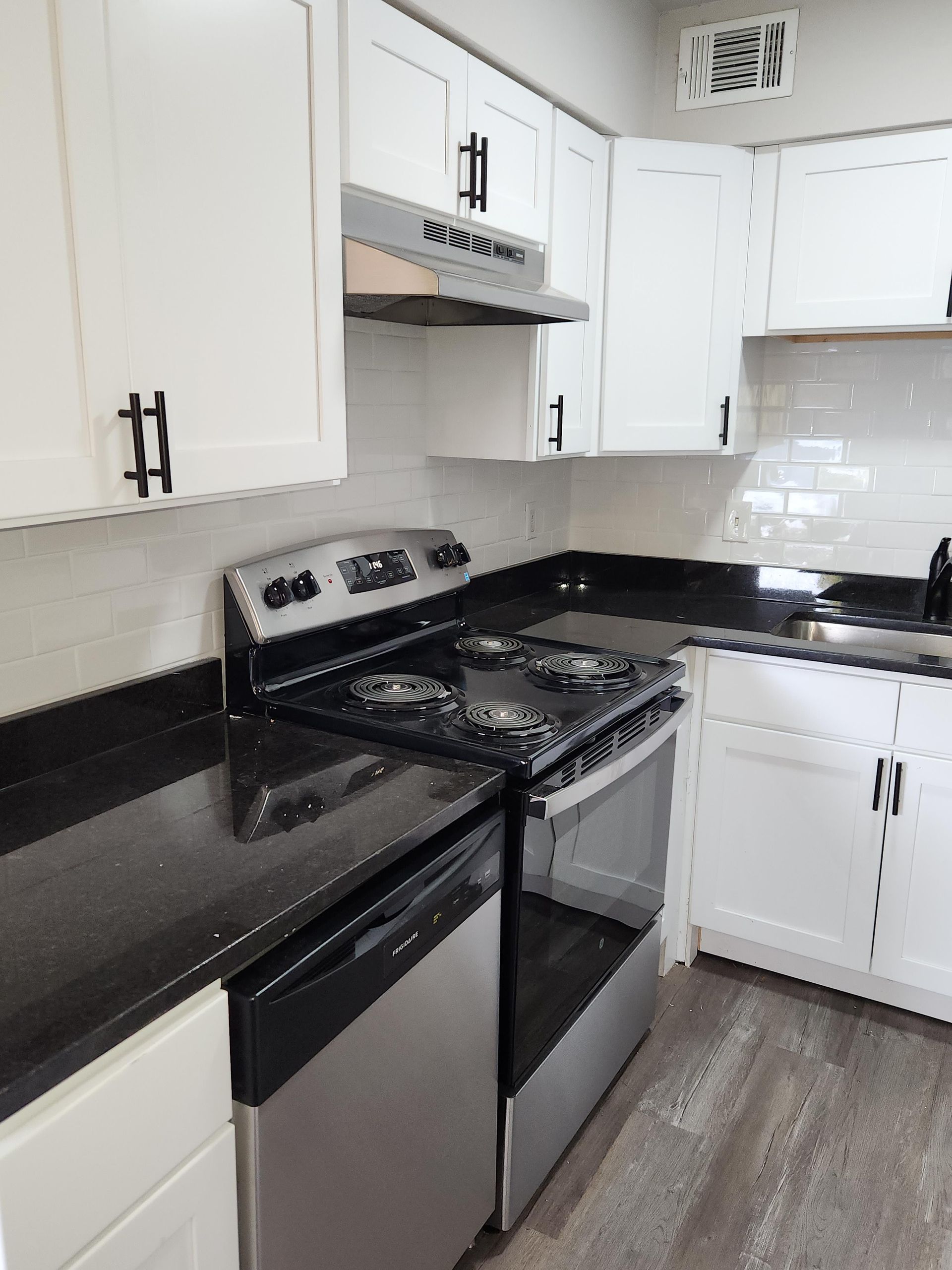 A kitchen with white cabinets , a black refrigerator , a black stove , and a sink.