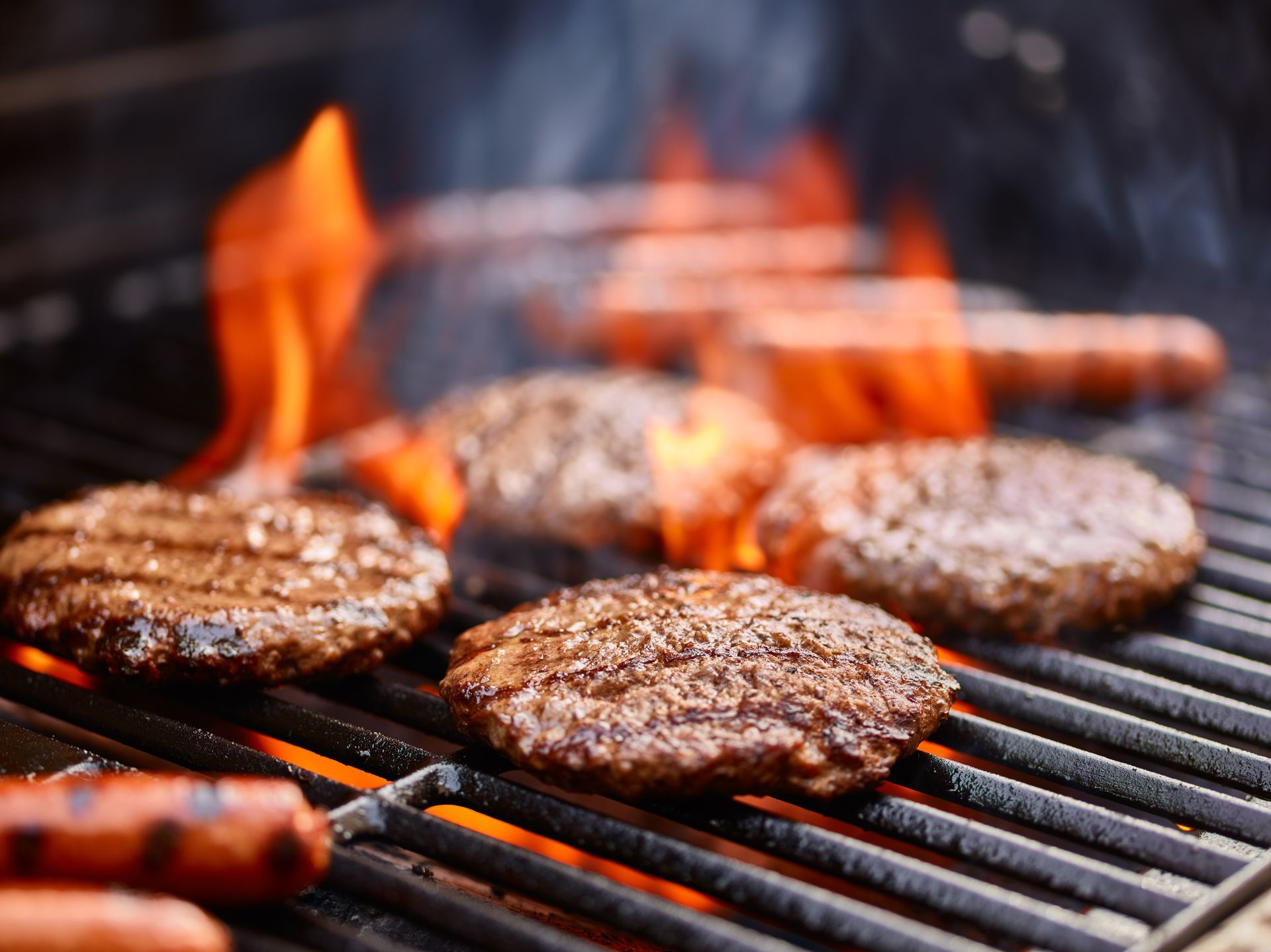 hamburgers and hot dogs are cooking on a grill.