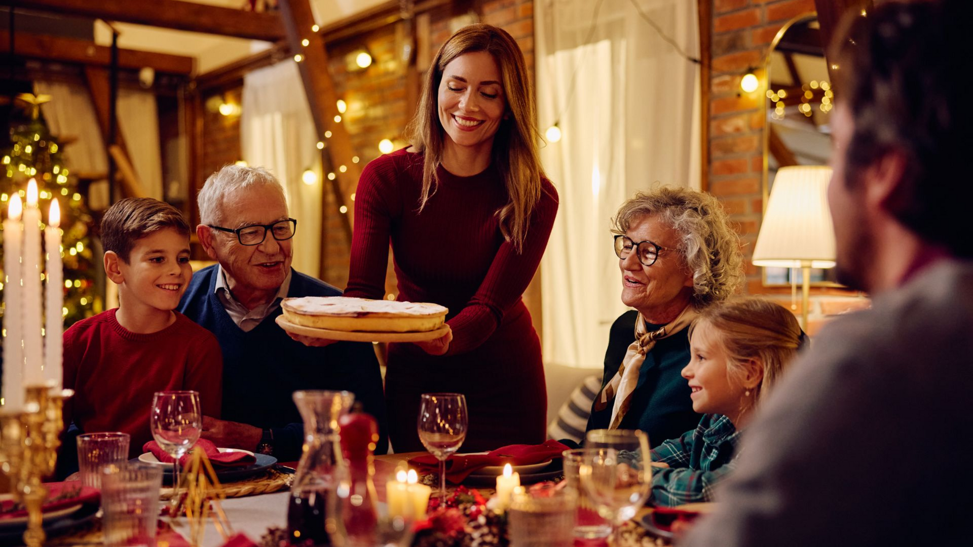 Woman serving a pie at a holiday dinner table with family, warm lighting.
