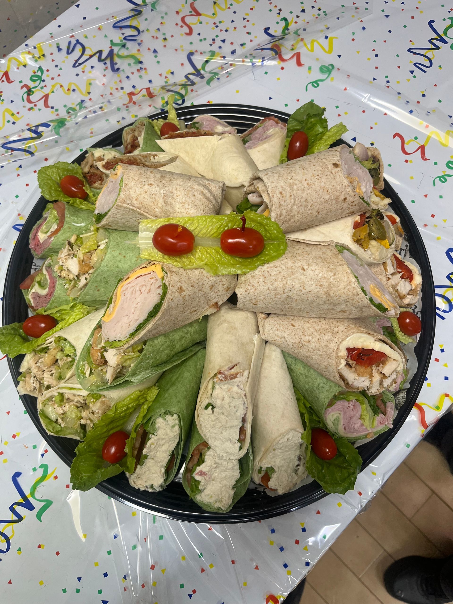 A tray of wraps and tomatoes on a table.