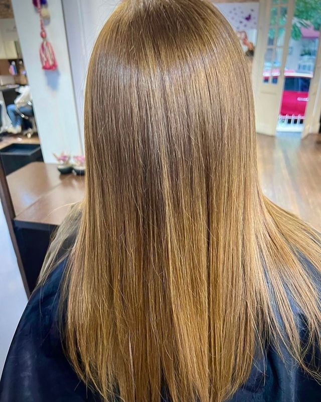 Una persona con cabello largo, liso y castaño oscuro está sentada en una silla de peluquería frente a un espejo.