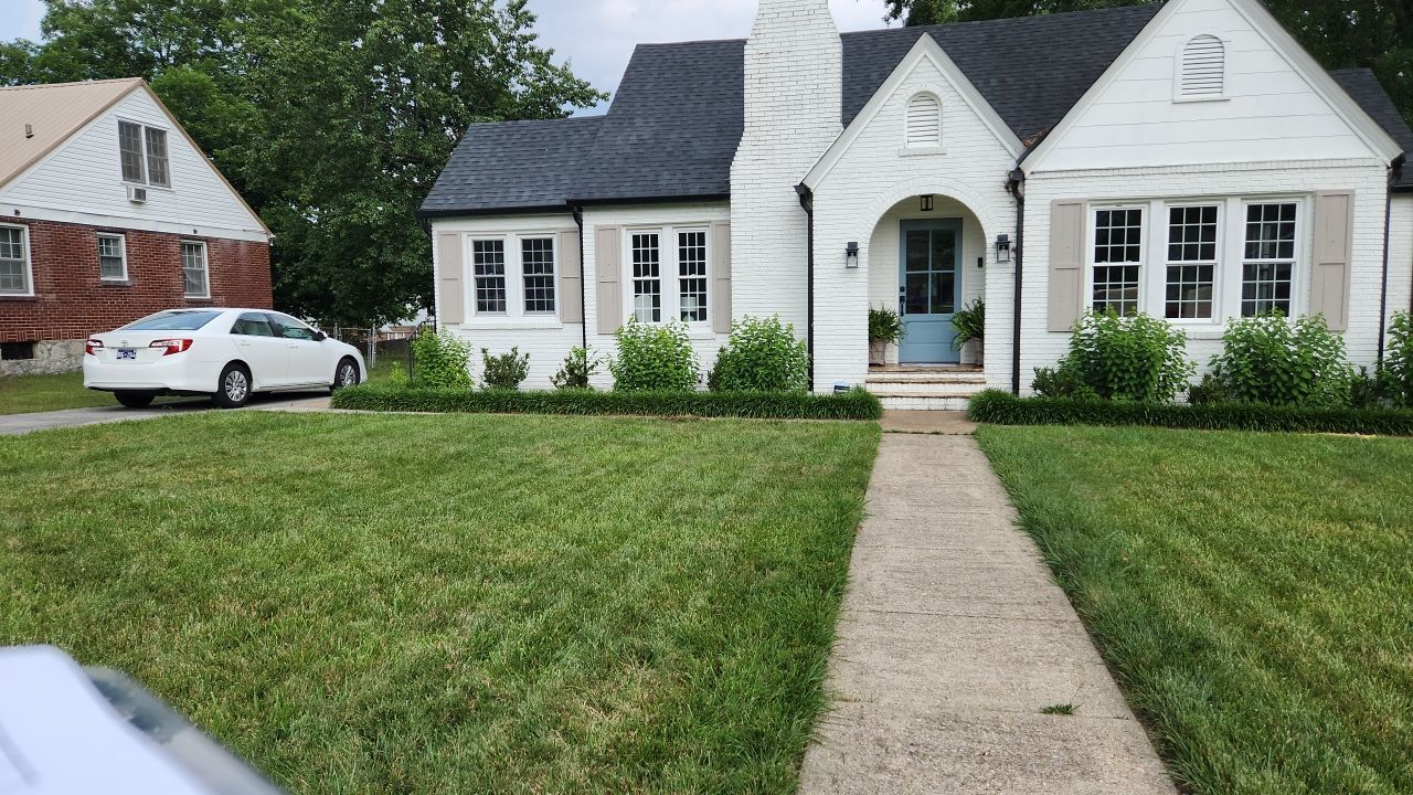 A white car is parked in front of a white house.