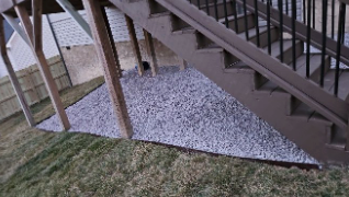 A set of stairs leading up to a deck with gravel on the ground.