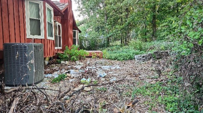 A red house with a black air conditioner in the backyard.