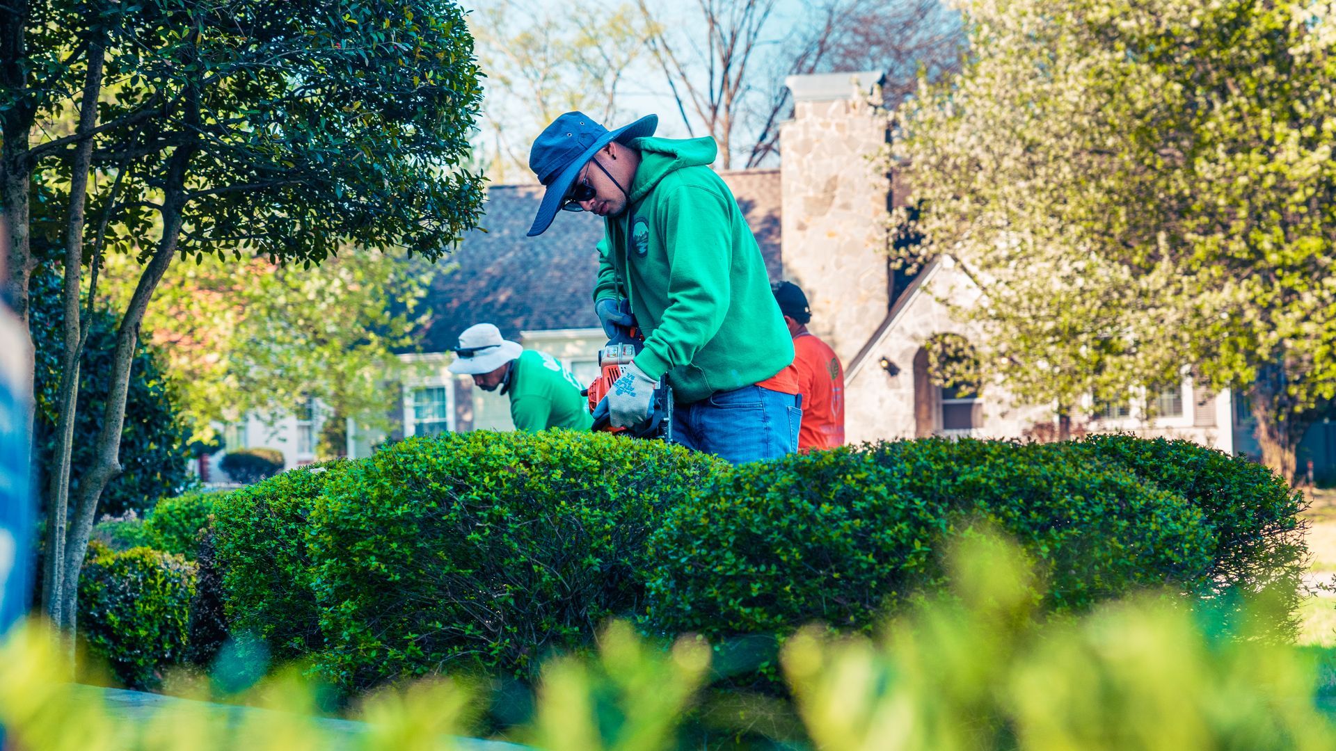 A man in a green jacket is trimming a bush