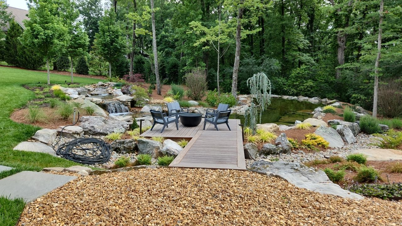 A wooden bridge leading to a patio with chairs and a fire pit.