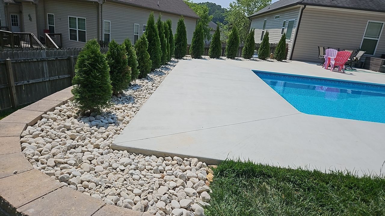 A large in ground swimming pool and patio is surrounded by rocks and trees