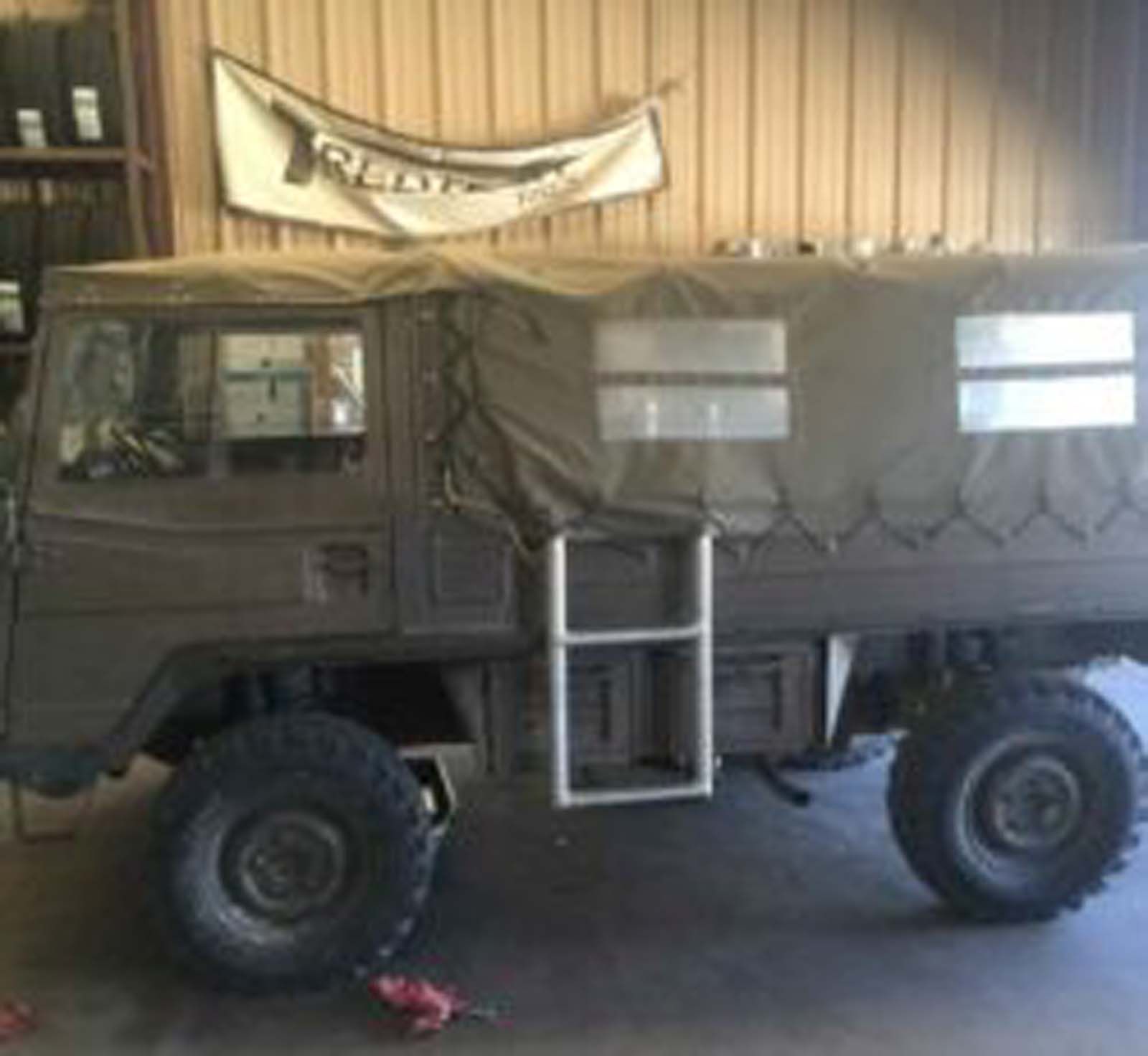A military truck with a ladder is parked in a garage.