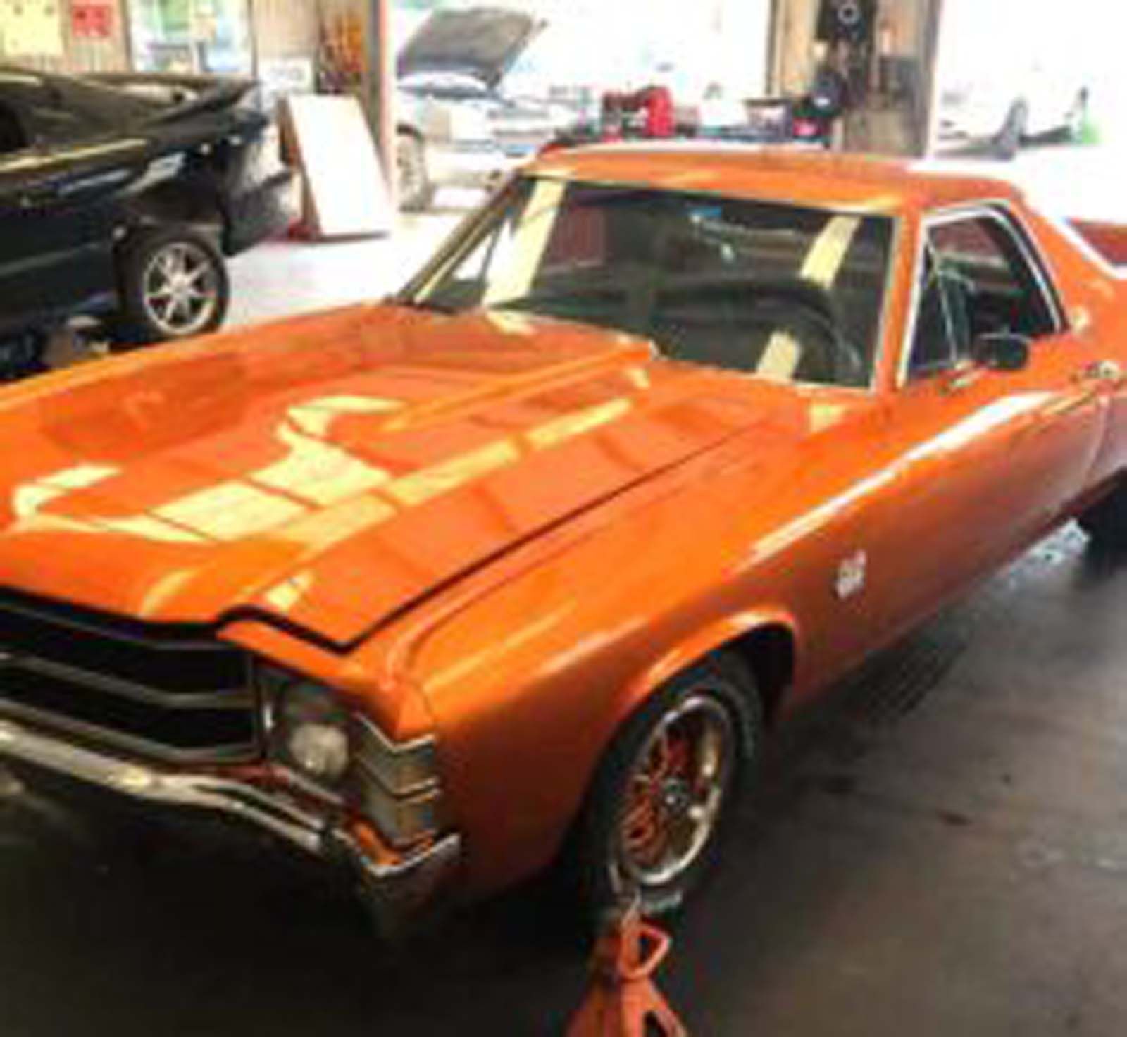 An orange car is parked in a garage with the hood up.