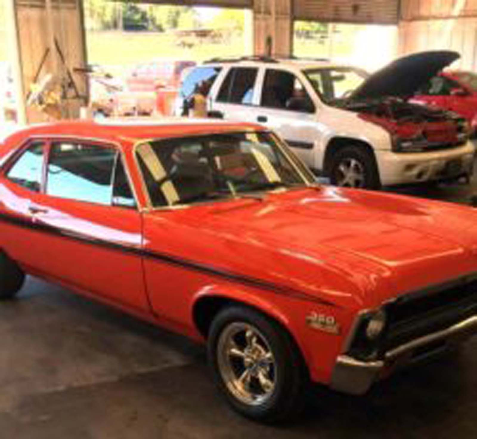 A red car is parked in a garage with other cars.