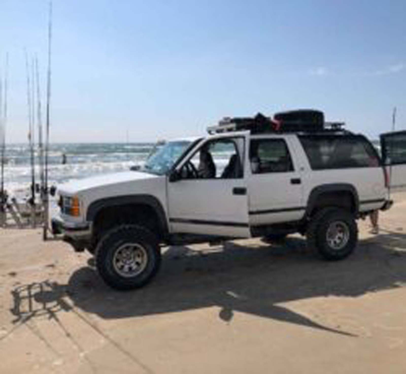 A white suv is parked on the beach next to the ocean.