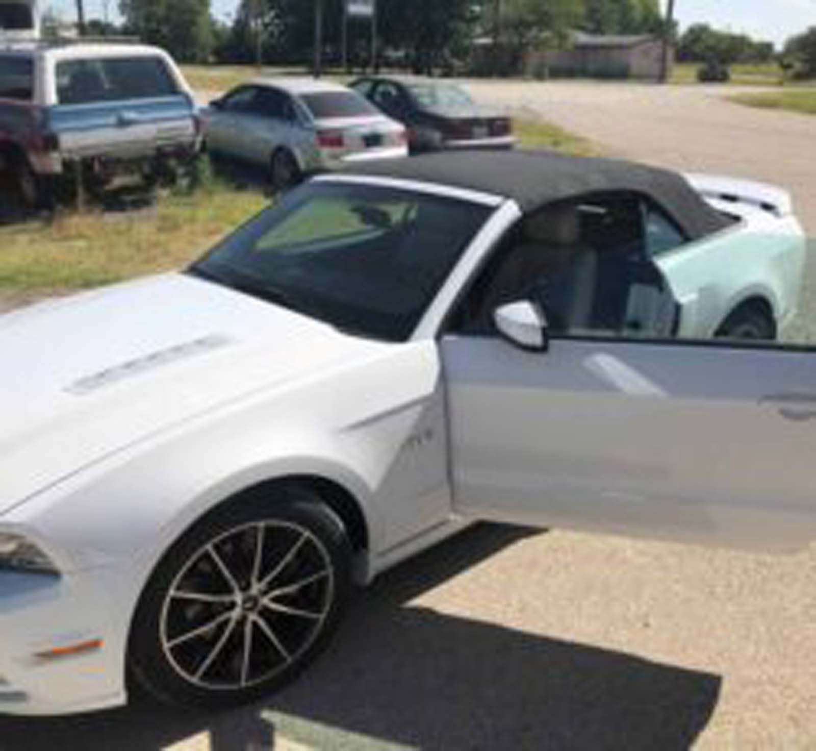 A white convertible mustang is parked in a parking lot with its door open.