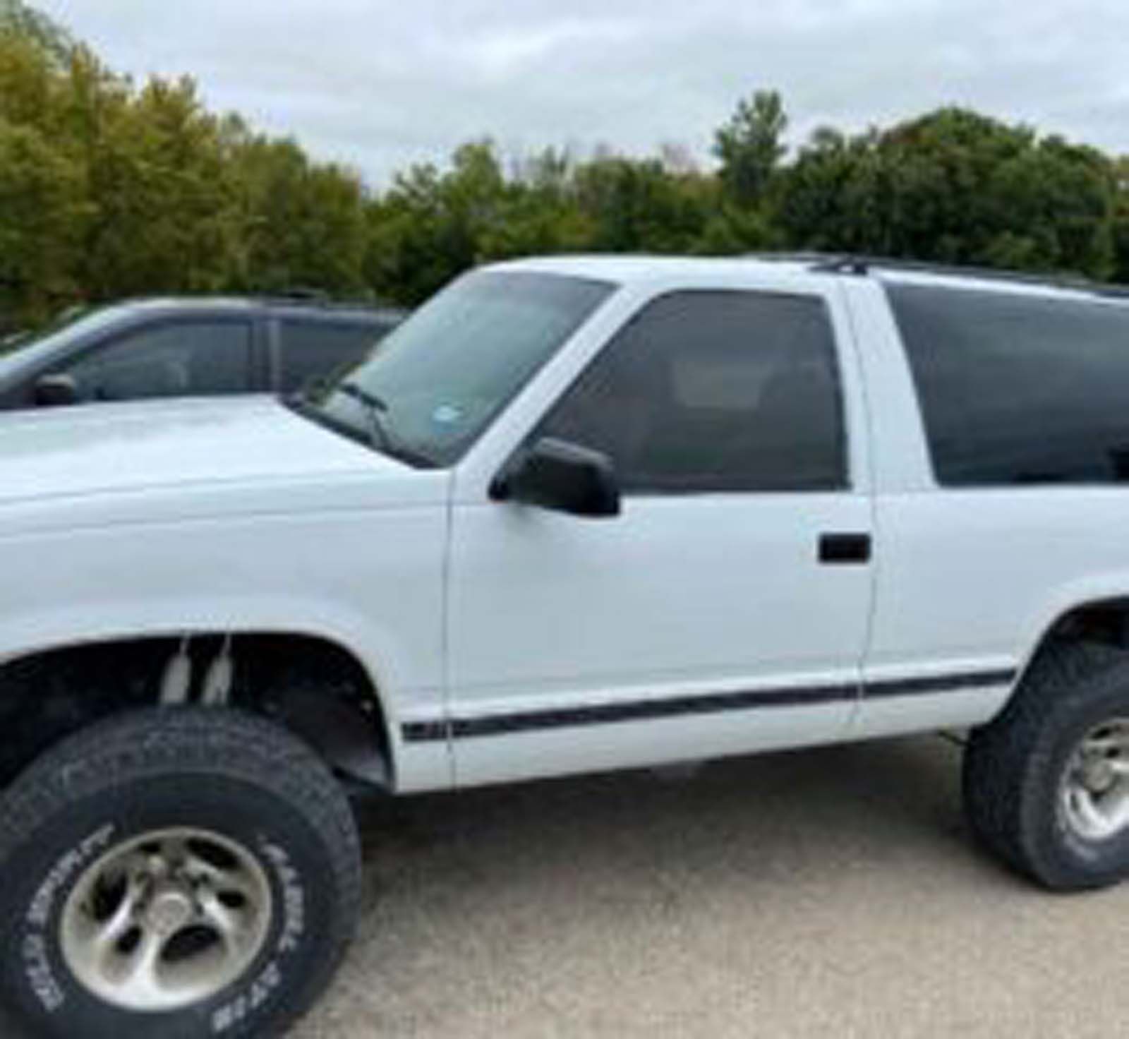 A white truck with black tires is parked on the side of the road.