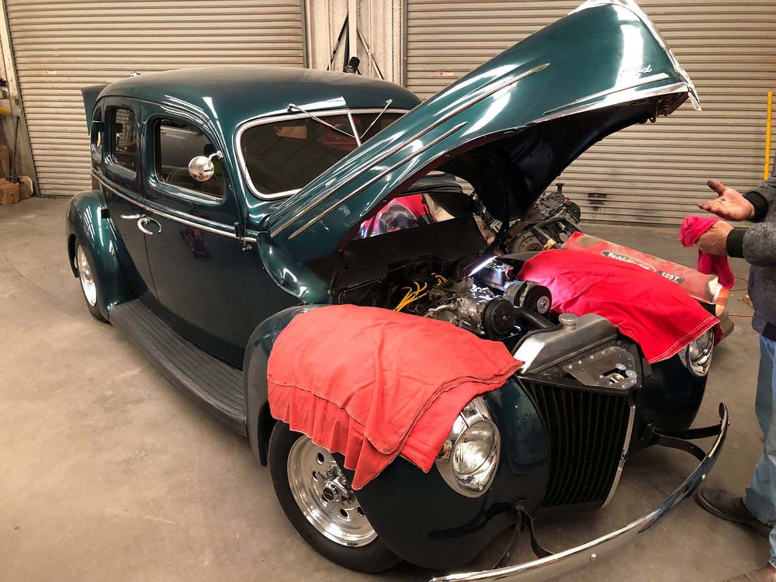 A green car with the hood open is being worked on in a garage.