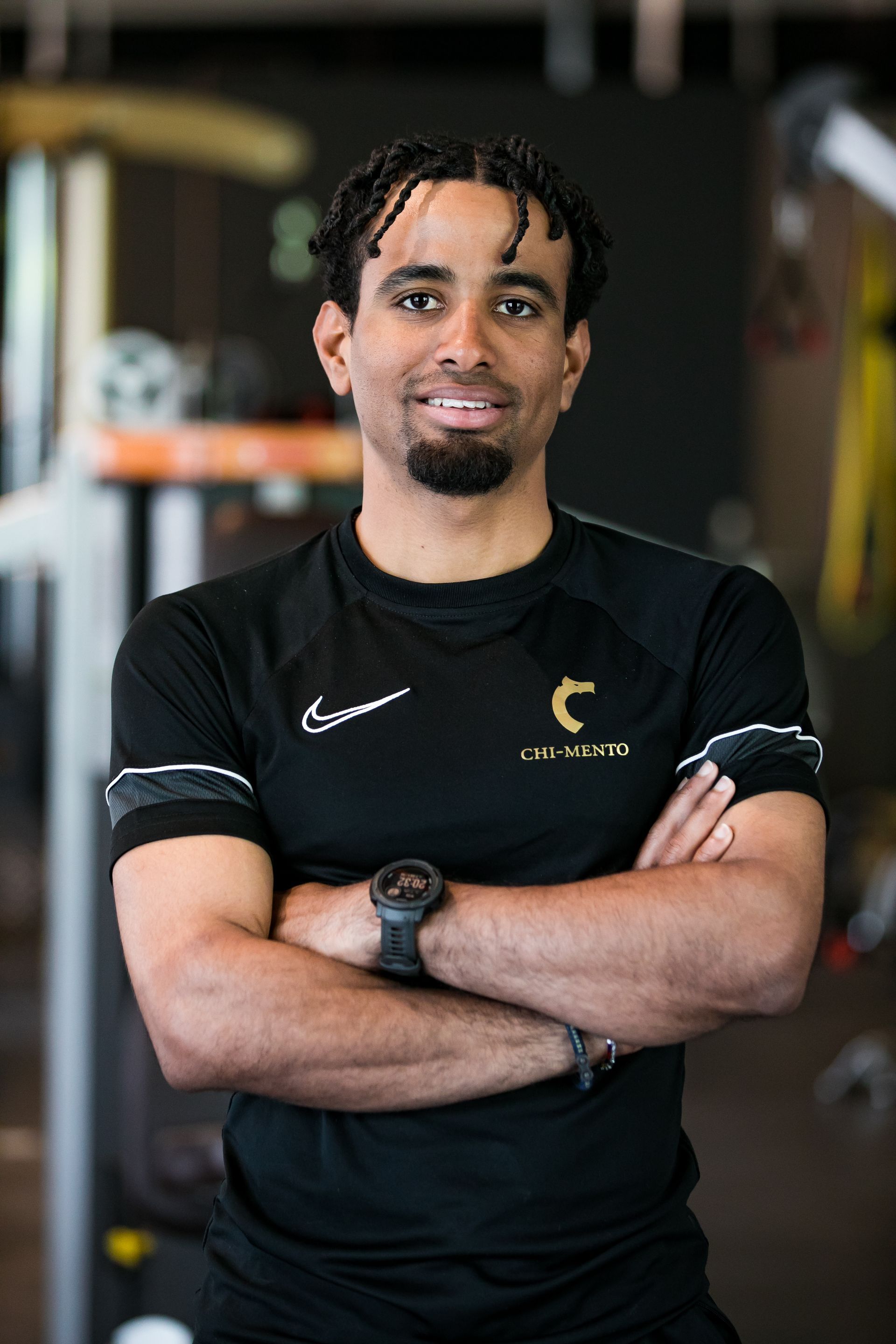 Een man in een zwart shirt staat met zijn armen over elkaar in een sportschool.