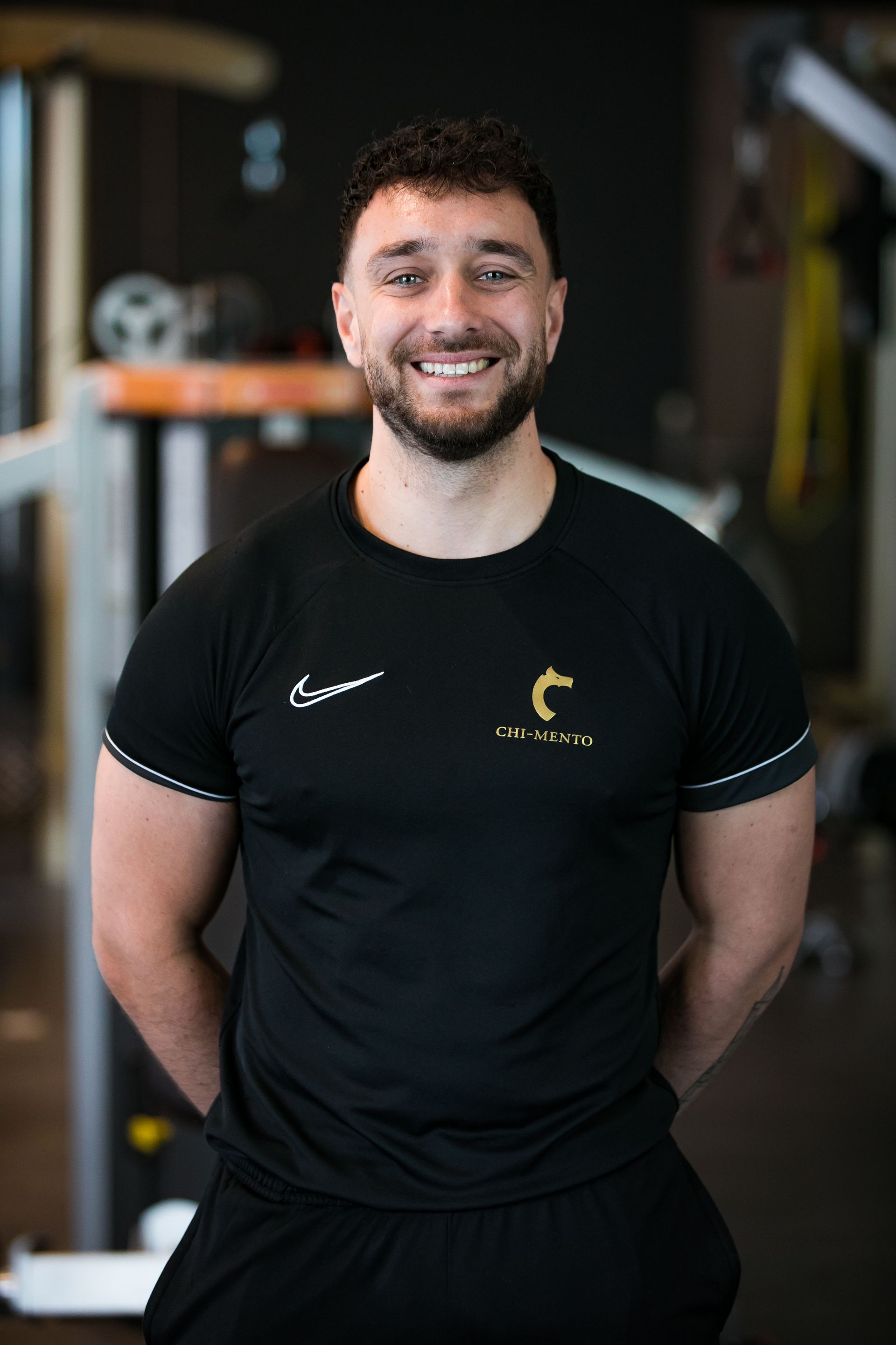 Een man met een baard draagt ​​een zwart shirt en lacht in een sportschool.