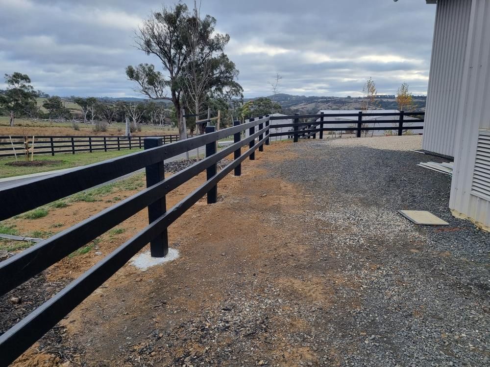 A Black Wooden Fence is Surrounding a Gravel Driveway — Ettles Rural Fencing in Alfredton, VIC