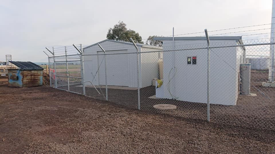 A Fence Surrounds A Row Of Buildings In A Dirt Field — Ettles Rural Fencing in Alfredton, VIC