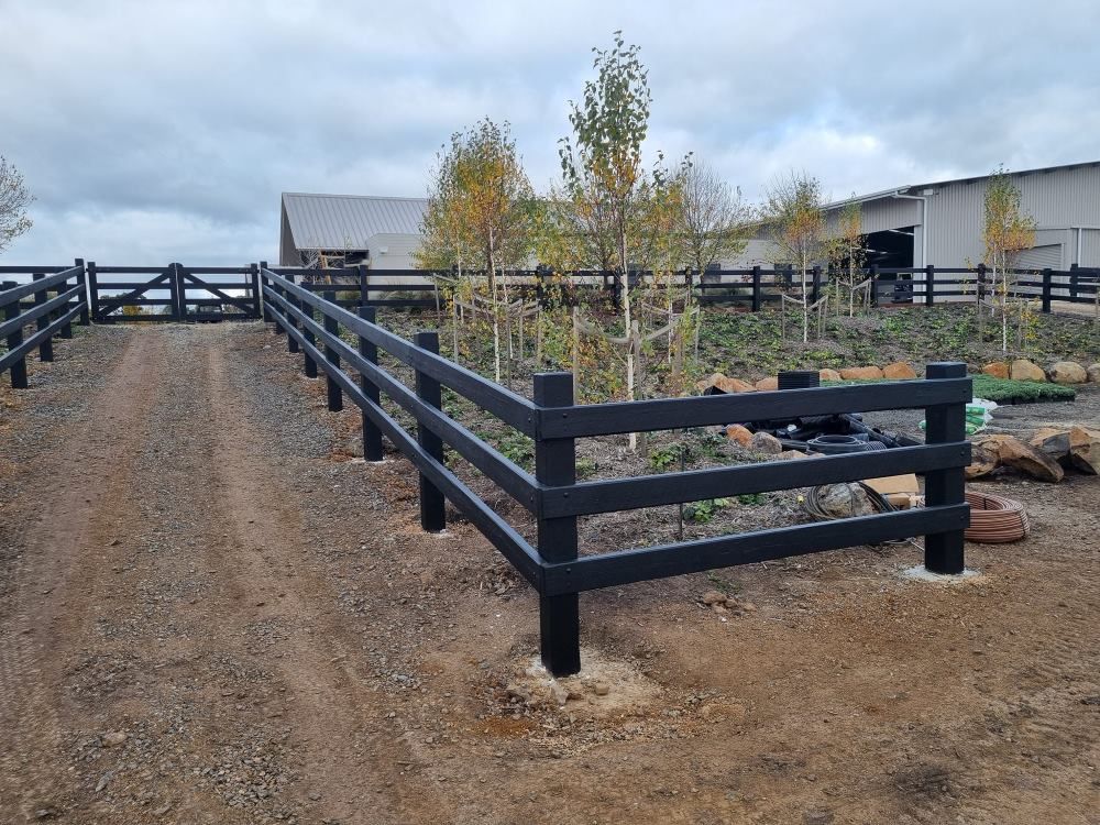A Black Wooden Fence Is Surrounding A Dirt Road — Ettles Rural Fencing in Alfredton, VIC