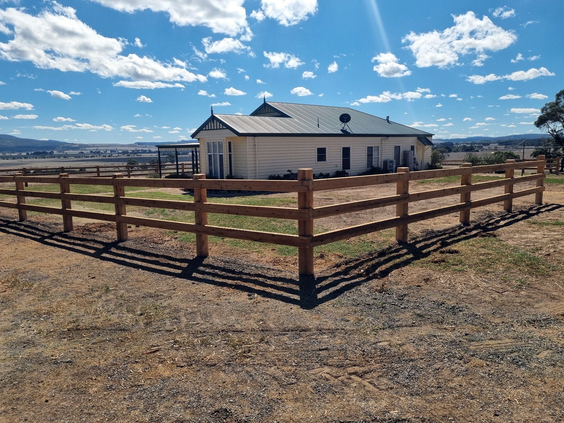 A Black Fence Surrounds A Dirt Road Leading To A Building — Ettles Rural Fencing in Alfredton, VIC