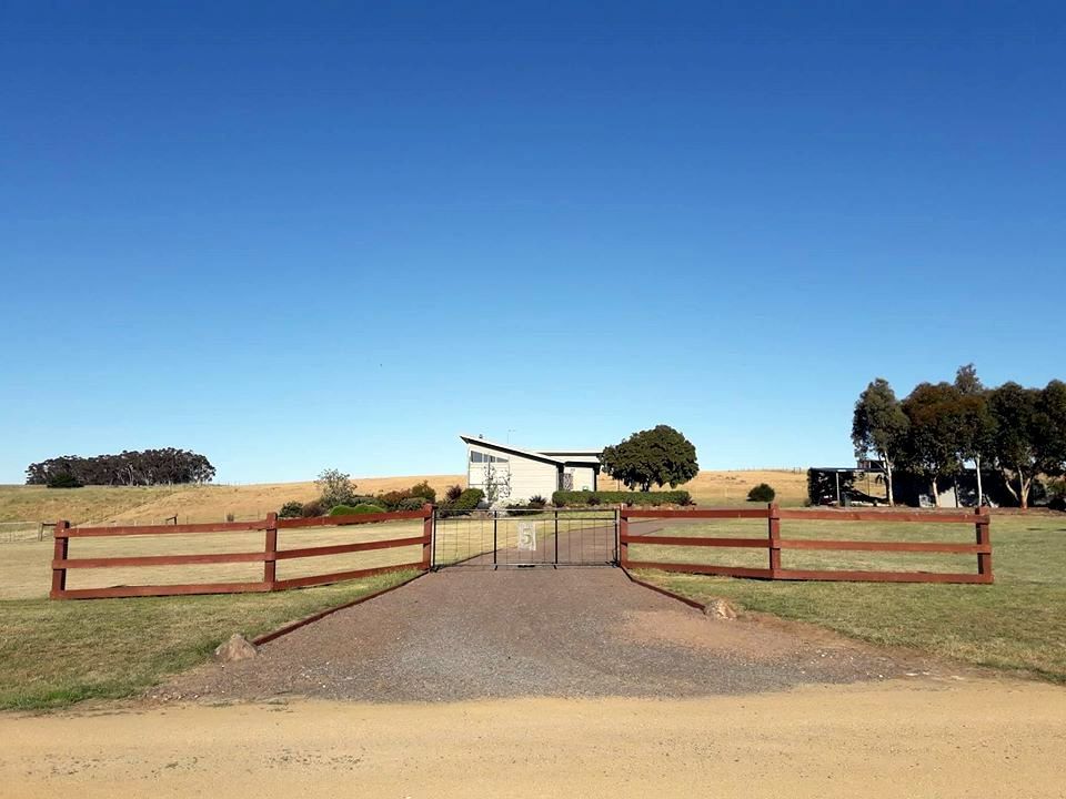 A Black Wooden Fence Surrounds a Gravel Driveway Next to a Building — Ettles Rural Fencing in Alfredton, VIC
