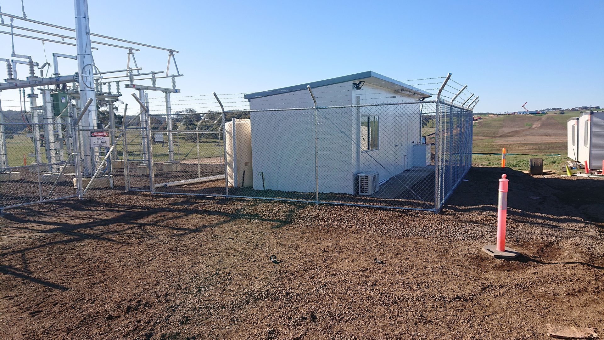 A Small White Building Behind a Chain Link Fence in a Dirt Field — Ettles Rural Fencing in Alfredton, VIC