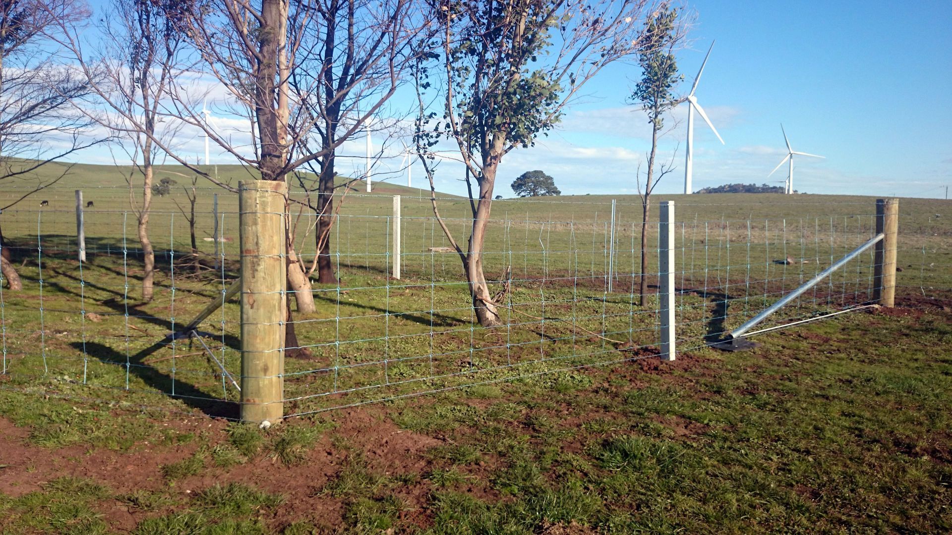 A Wooden Fence With a Metal Gate in Front of a Building — Ettles Rural Fencing in Alfredton, VIC